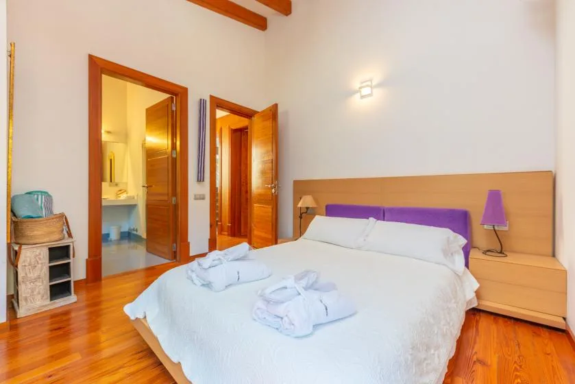 Un dormitorio con una cama, mesitas de noche y puertas de madera abiertas.