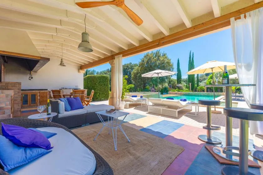 Una sala exterior cubierta se abre a un patio junto a la piscina con asientos y sombrillas.