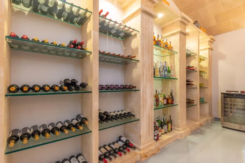 Una sala de almacenamiento de vino con botellas en estantes y un enfriador con puerta de vidrio.