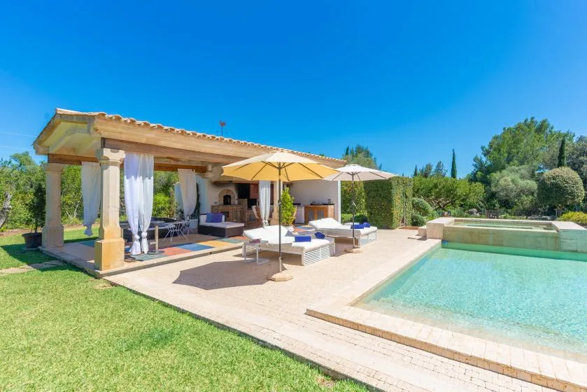 Un patio junto a una piscina cuenta con asientos a la sombra y un jardín.