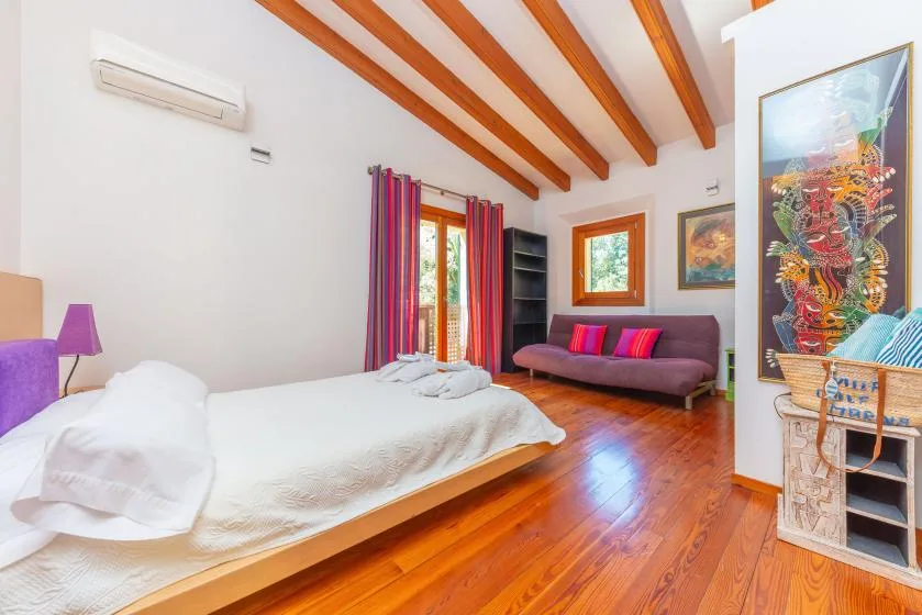 Dormitorio con una cama, un sofá morado y vigas de madera a la vista.