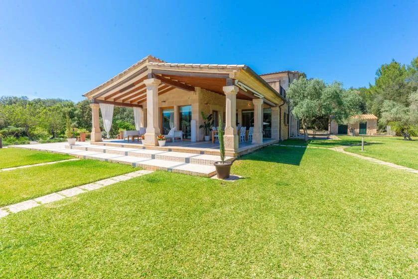 Una casa con un patio cubierto y césped bajo un cielo azul despejado.