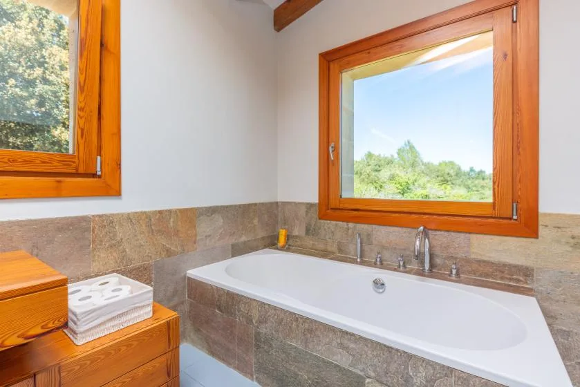Un baño con una bañera bajo una ventana grande.