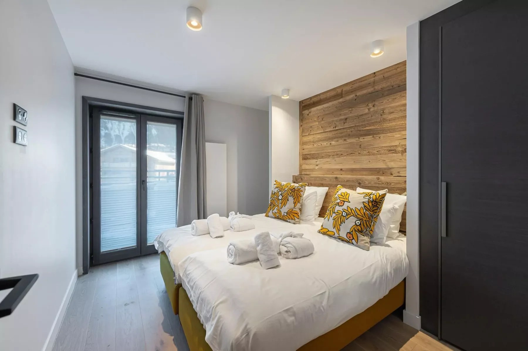 A bedroom with white bedding and patterned pillows beside a wood-paneled wall.