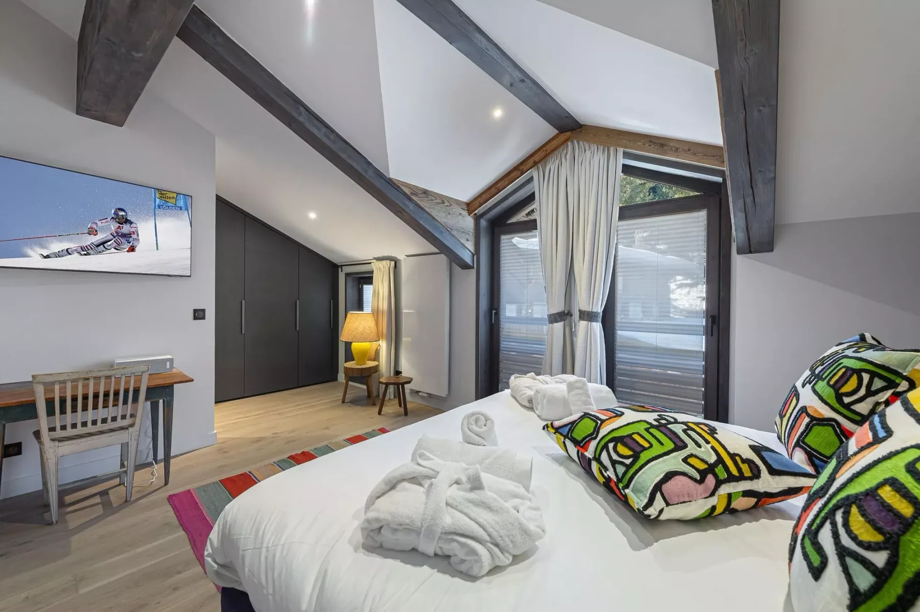 Un dormitorio con una cama, almohadas estampadas y vigas expuestas en el techo.
