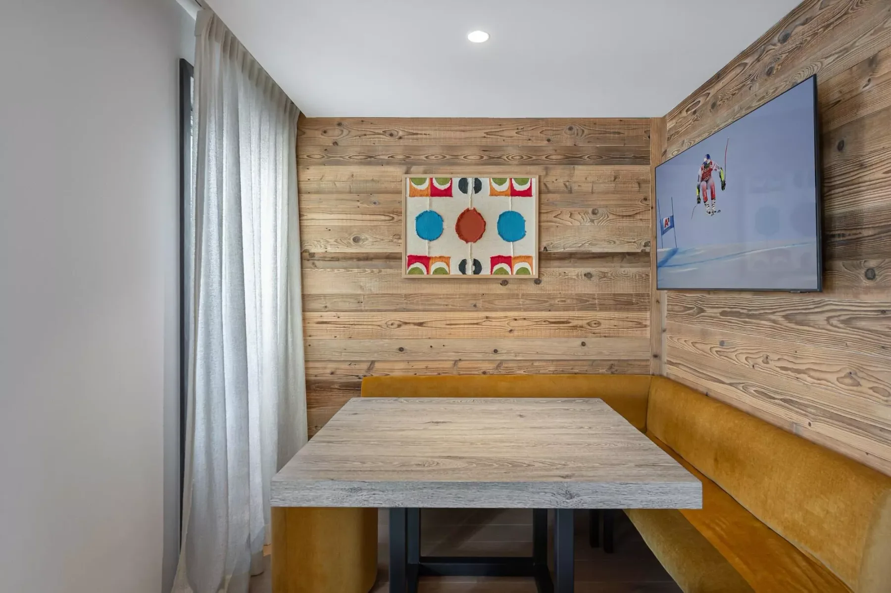 Un rincón de comedor con mesa, asientos acolchados y paredes revestidas de madera.