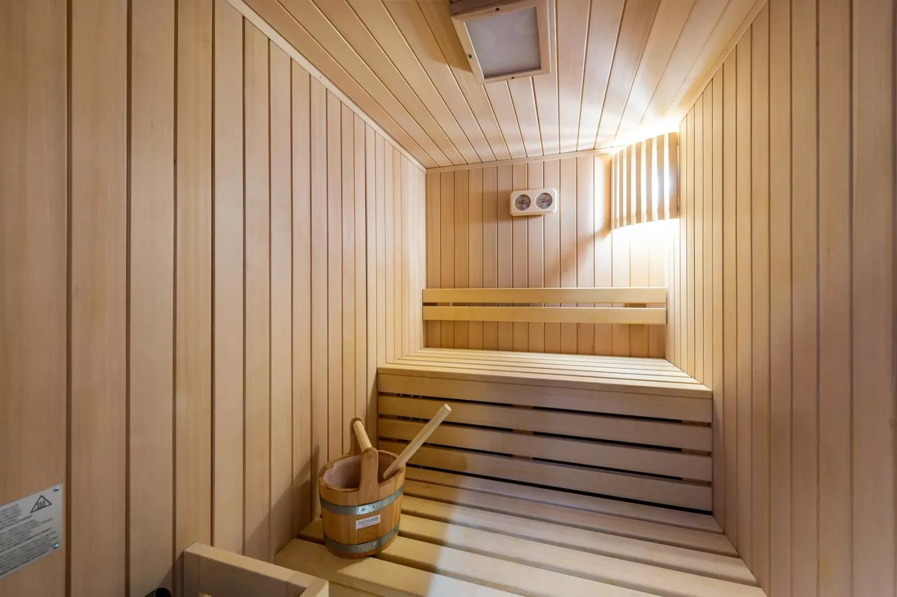 Una sauna revestida de madera con asientos escalonados y un pequeño cubo.