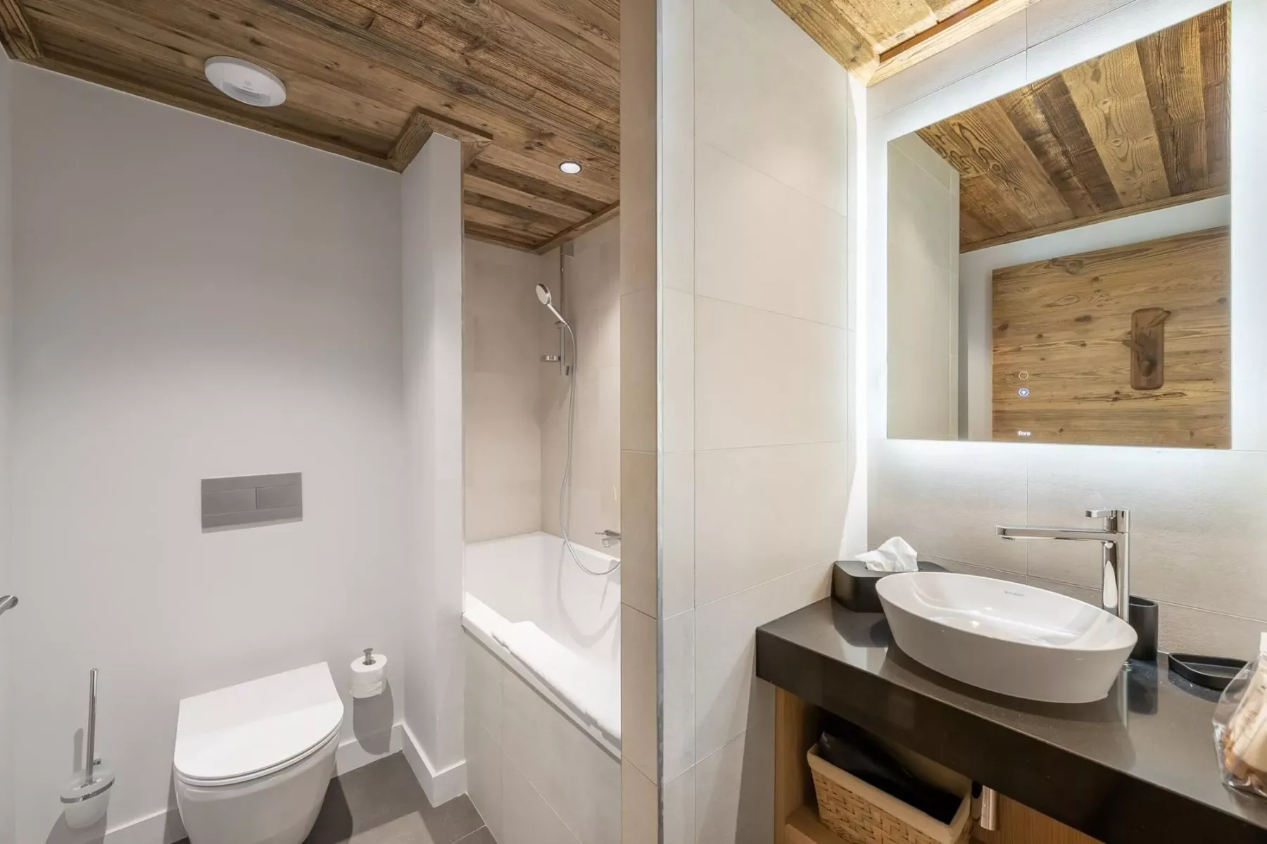 A bathroom with a toilet, bathtub, and sink beneath a large mirror.