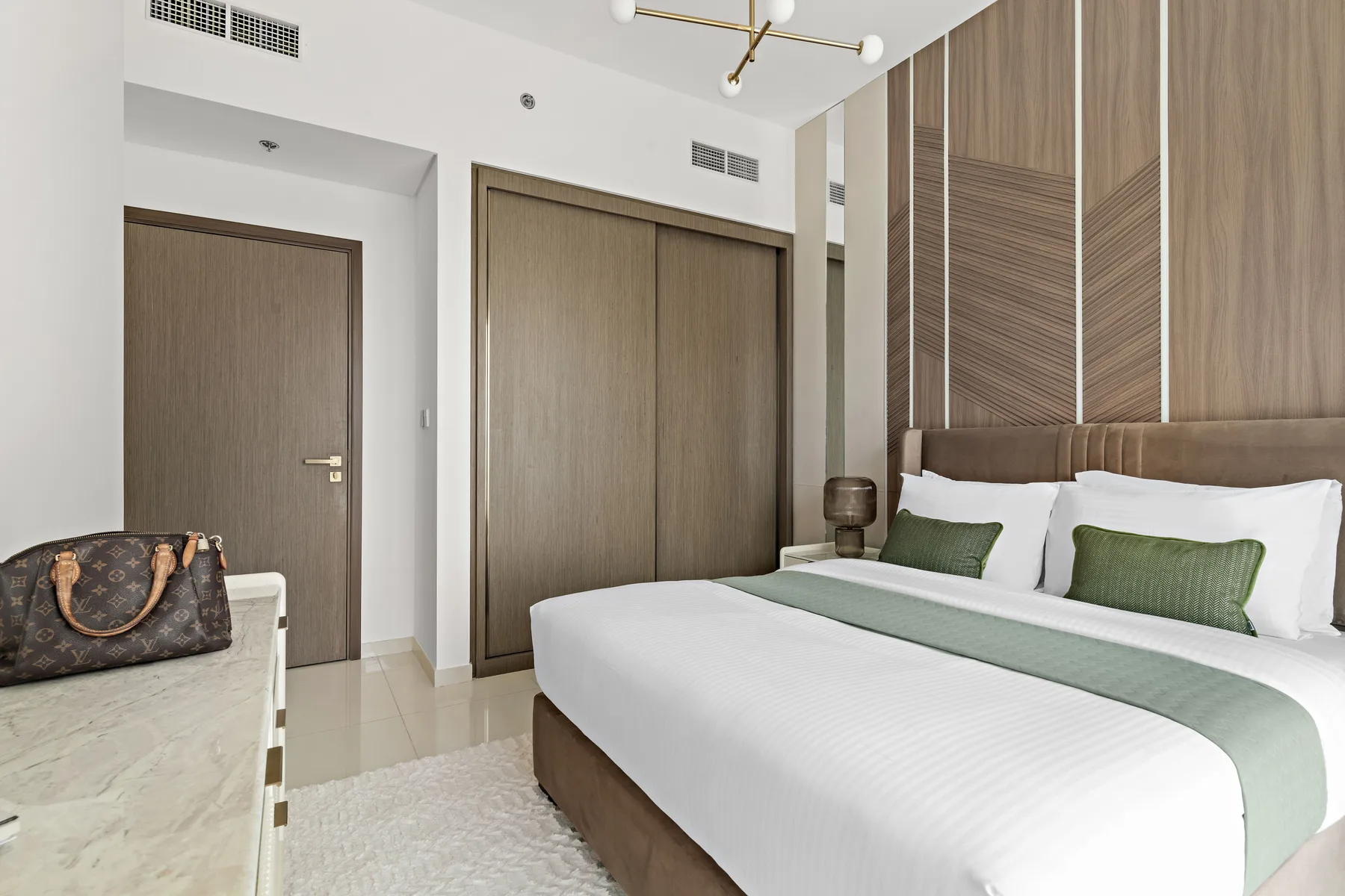 Un dormitorio con una cama grande, detalles verdes en la ropa de cama y paredes revestidas de madera.