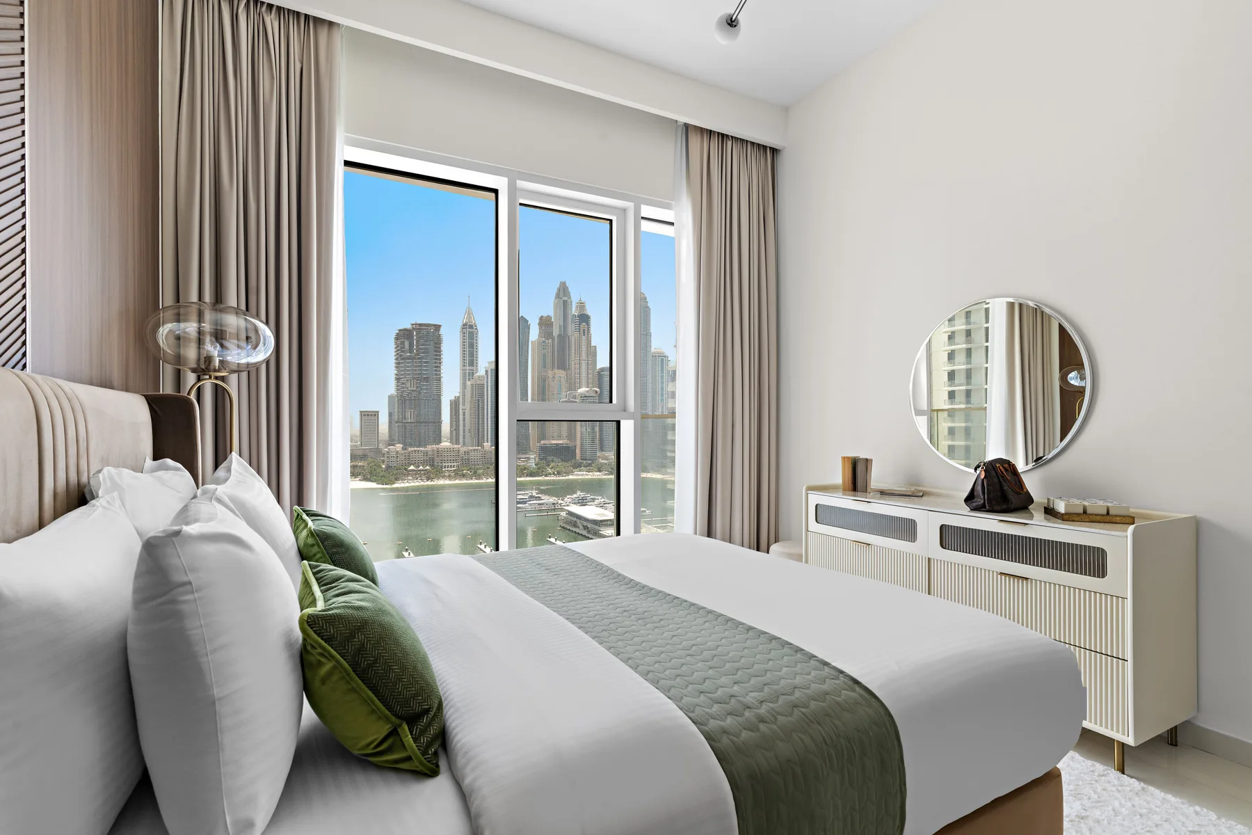 Un dormitorio luminoso con una cama ordenada y vistas de la ciudad por las ventanas.