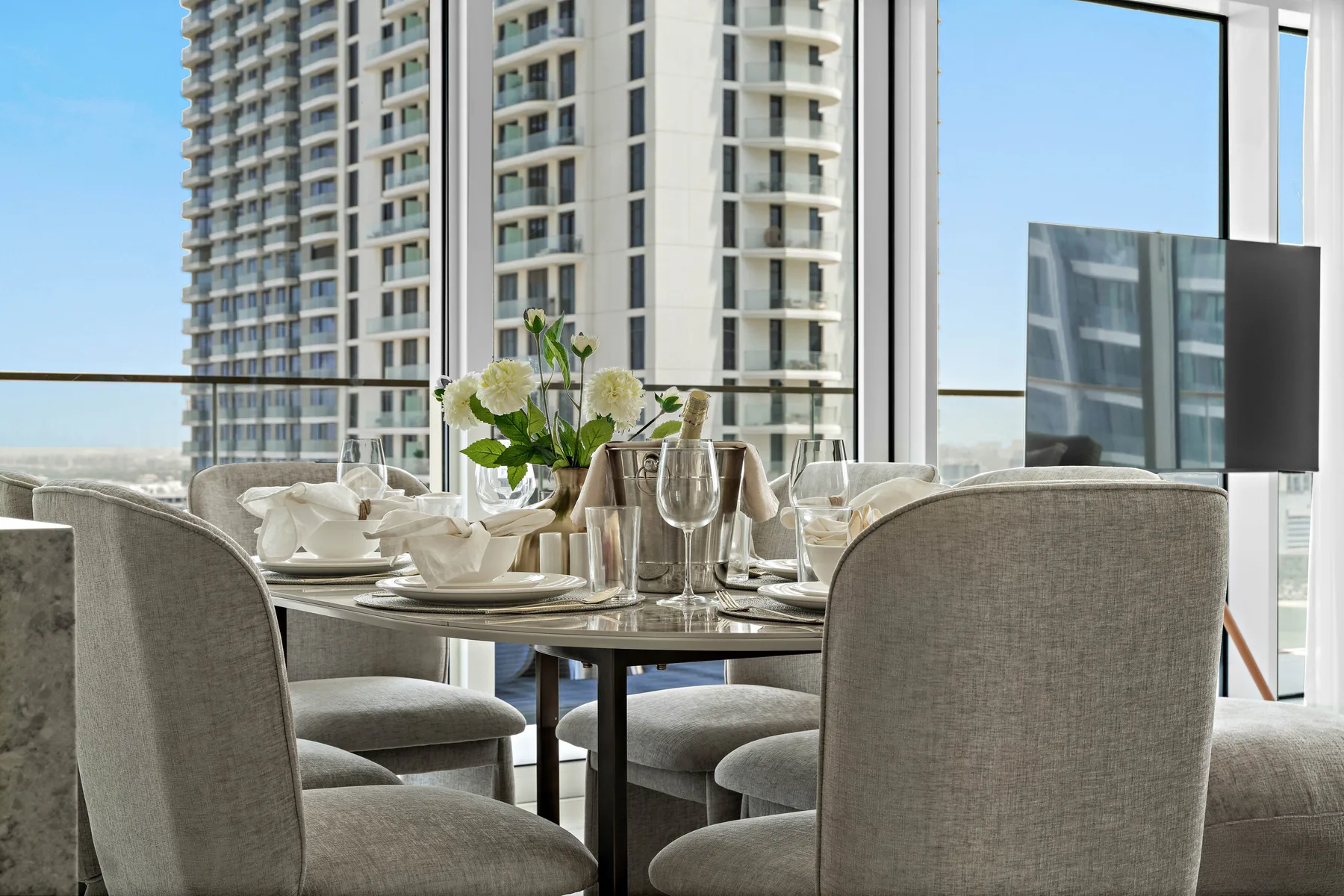 Comedor con la mesa puesta y ventanales con vistas a edificios cercanos.
