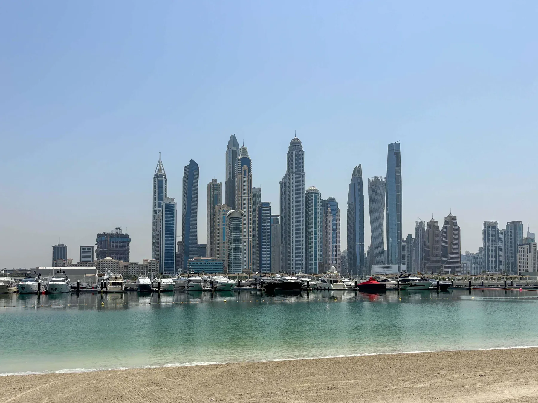 Un horizonte de edificios altos se alza detrás de una marina y una playa de arena.