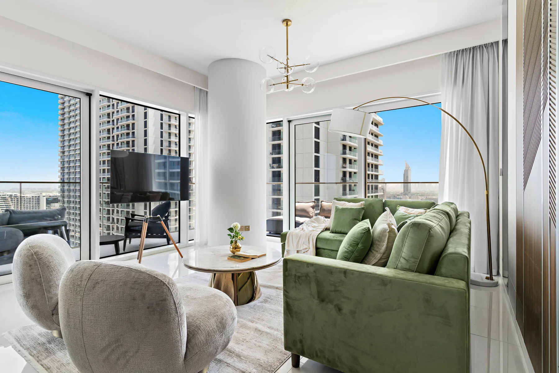 A bright living room with green seating and large windows overlooking neighboring buildings.