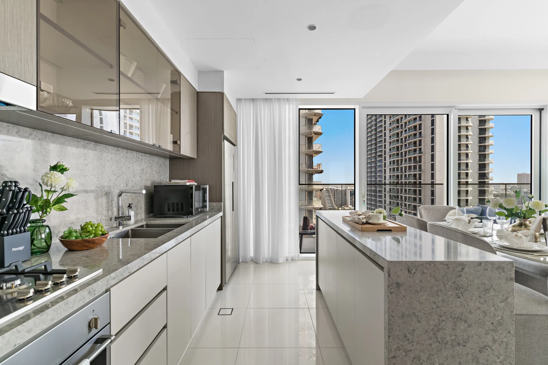 Una cocina moderna y luminosa con una isla central y grandes ventanales con vistas a edificios cercanos.