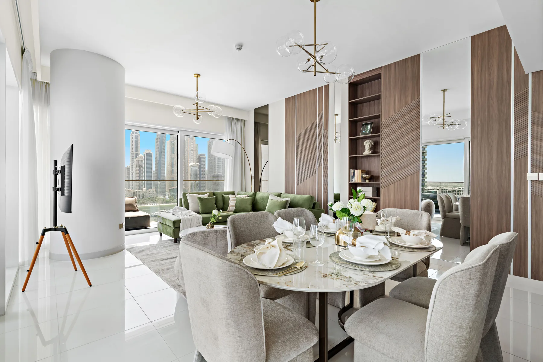 Un comedor luminoso con la mesa puesta y una sala junto a grandes ventanas.