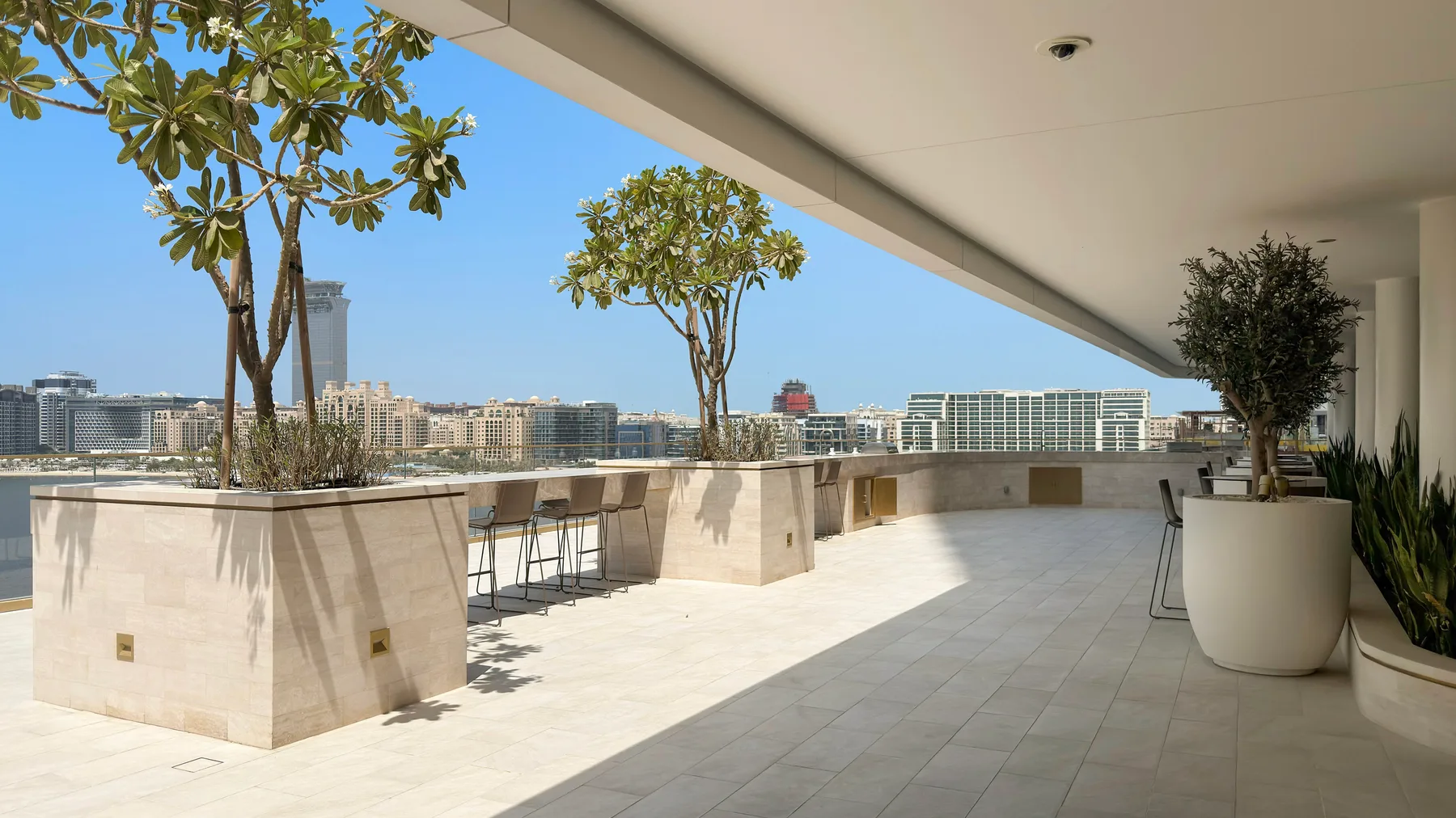 Una amplia terraza en la azotea con jardineras y asientos al aire libre da a edificios cercanos.