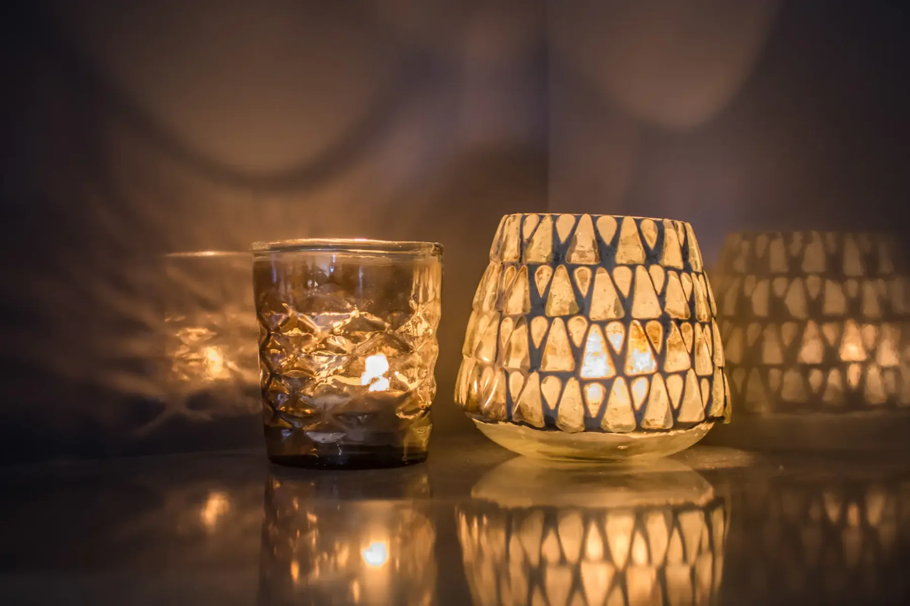 Un portavelas estampado y luminoso está junto a un vaso sobre una superficie reflectante.