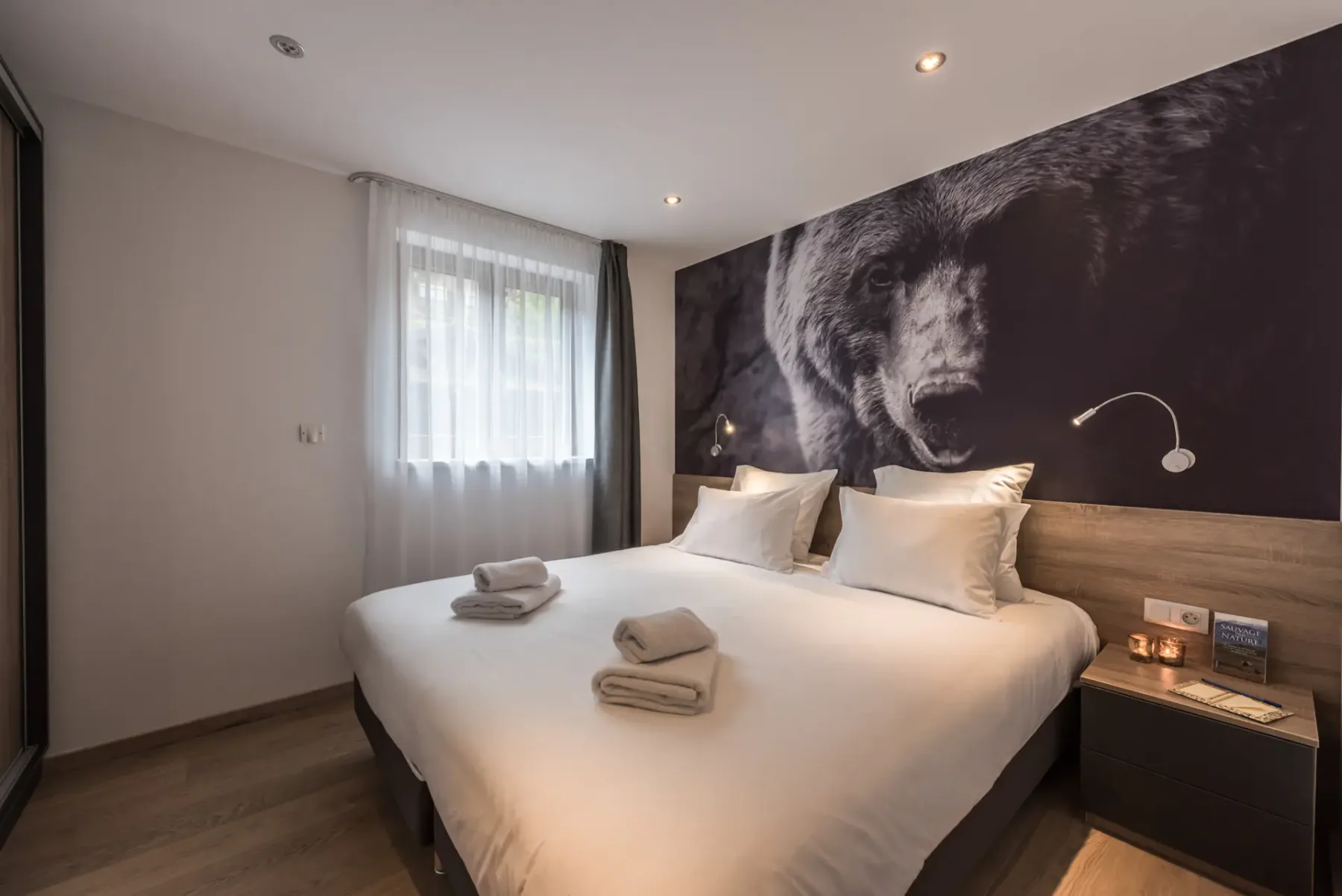 Un dormitorio con una cama bien hecha bajo un gran mural de un oso.