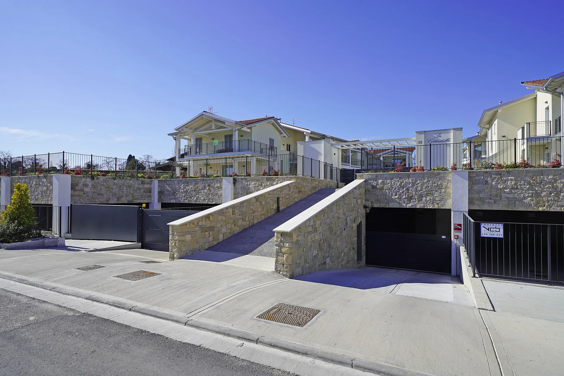 A row of modern homes stands above stone retaining walls and garage entrances.