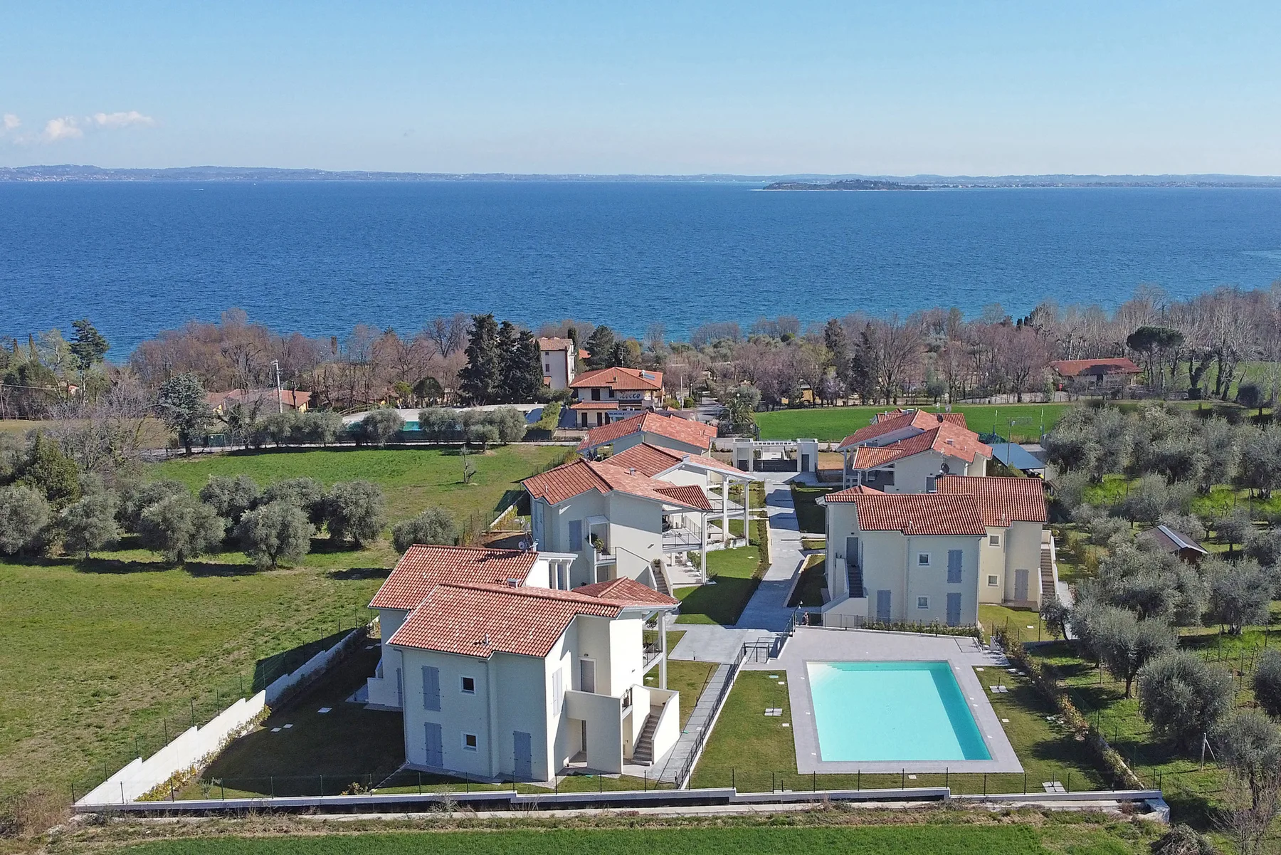Aerial view of homes with red-tiled roofs beside a swimming pool and the sea.