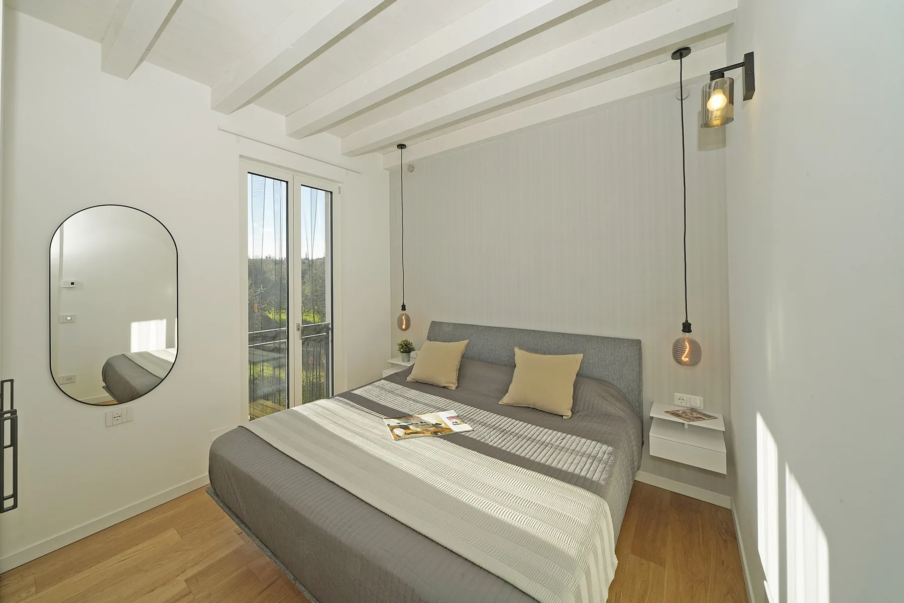 A bright bedroom with a large bed, pendant lights, and tall windows.