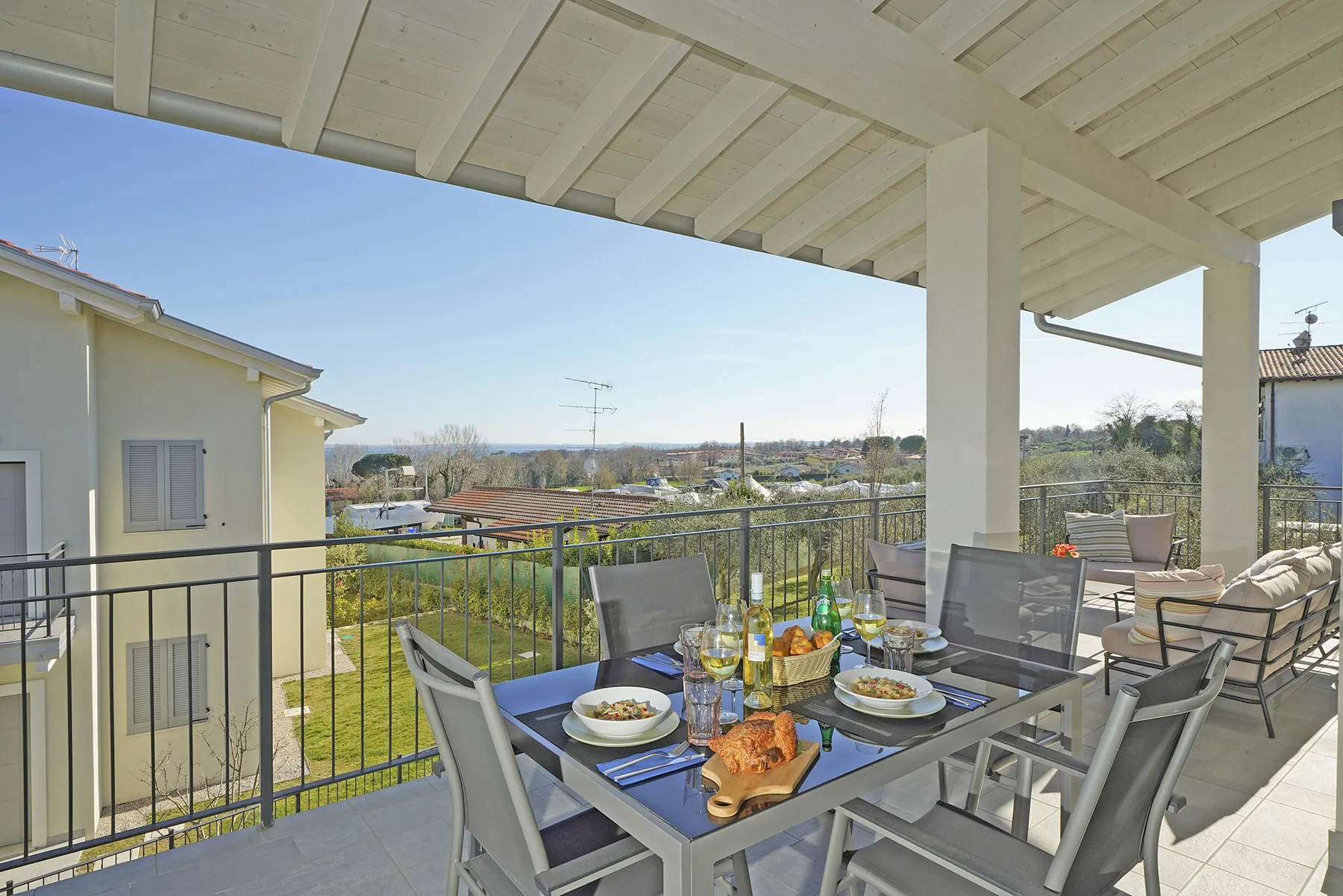 A covered outdoor dining area with a table and seating overlooking greenery.