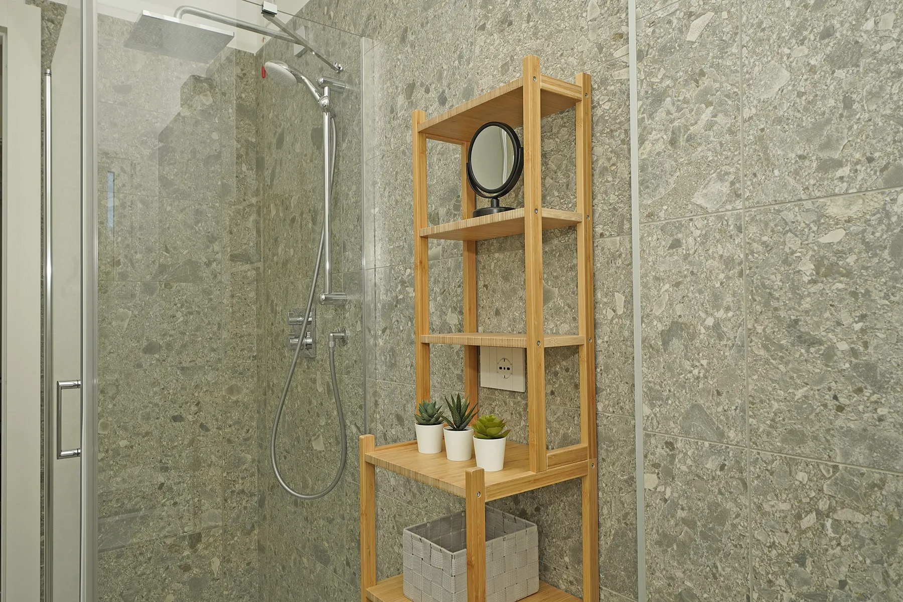 A tiled bathroom shower beside a wooden shelving unit with plants.