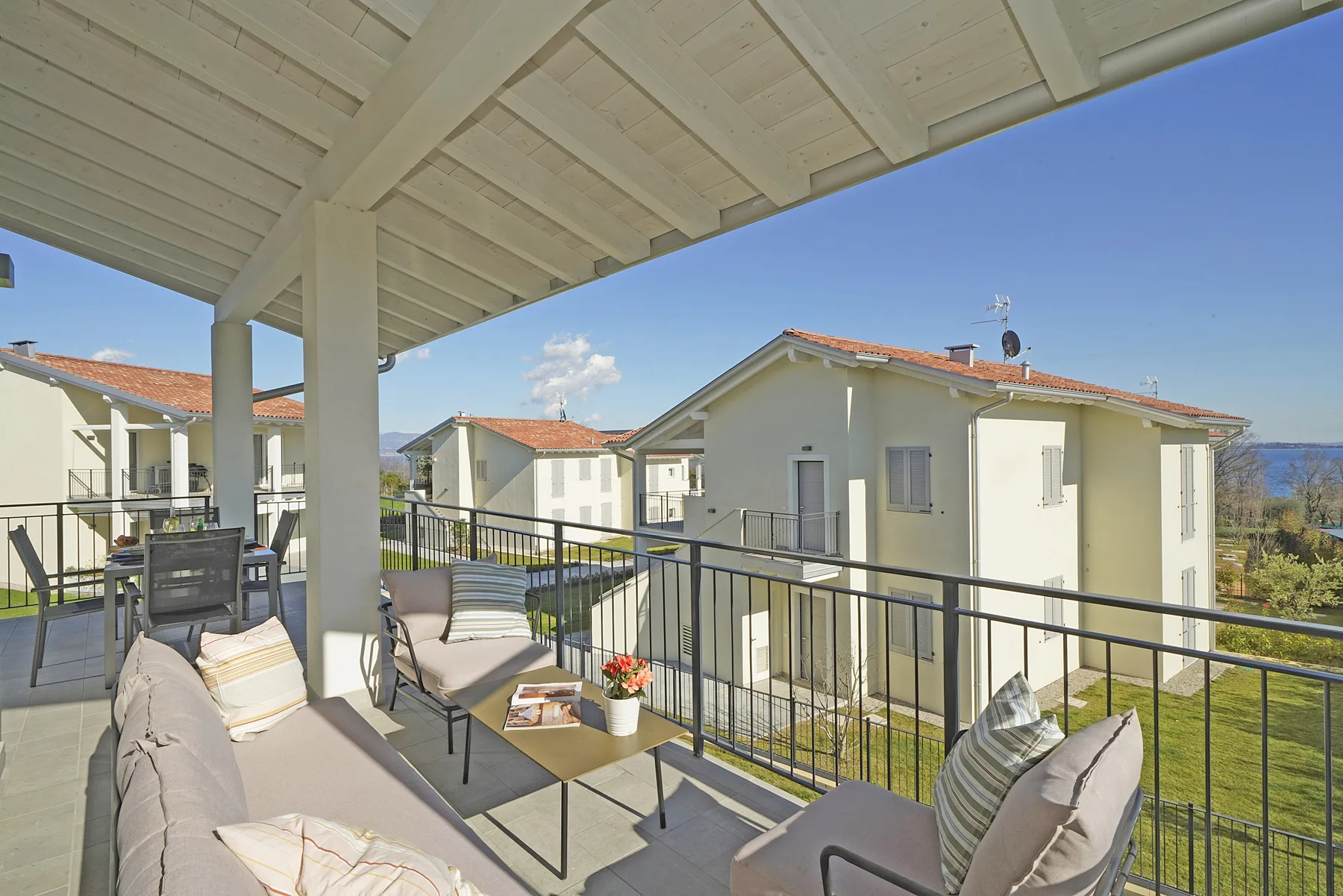 A covered balcony with outdoor seating overlooks neighboring houses and a clear blue sky.