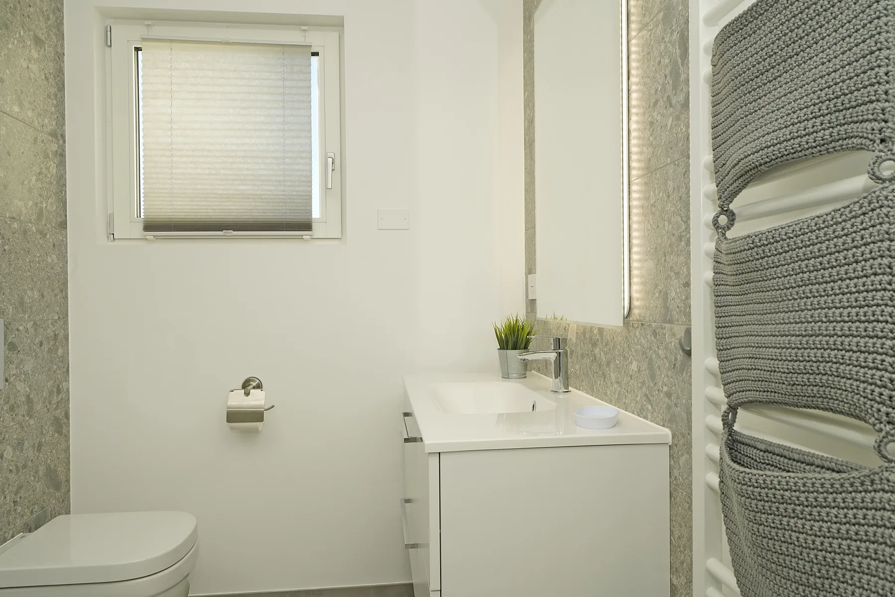 A bright bathroom with a vanity, toilet, and towel radiator.