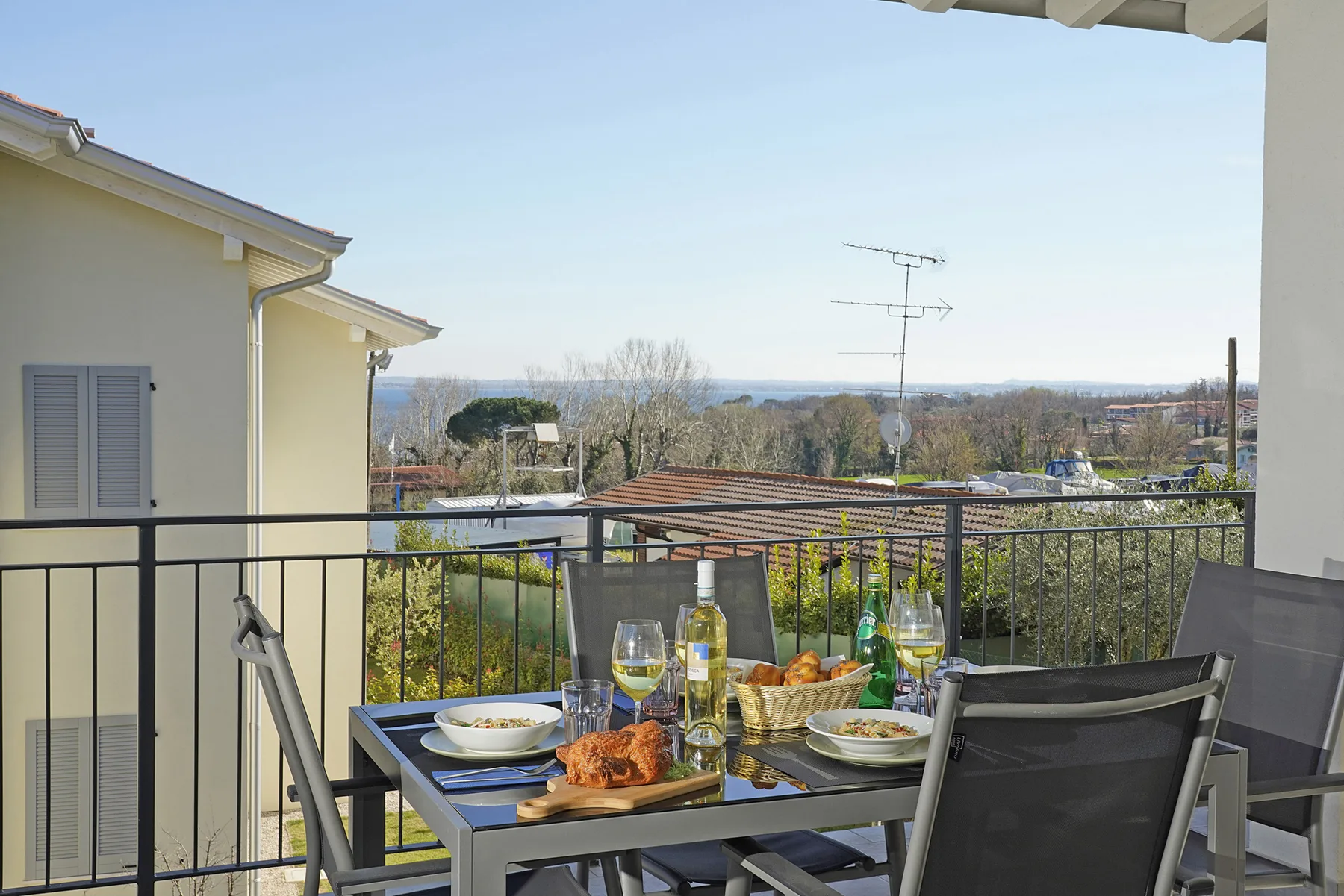 A balcony dining area overlooks surrounding greenery and distant rooftops.