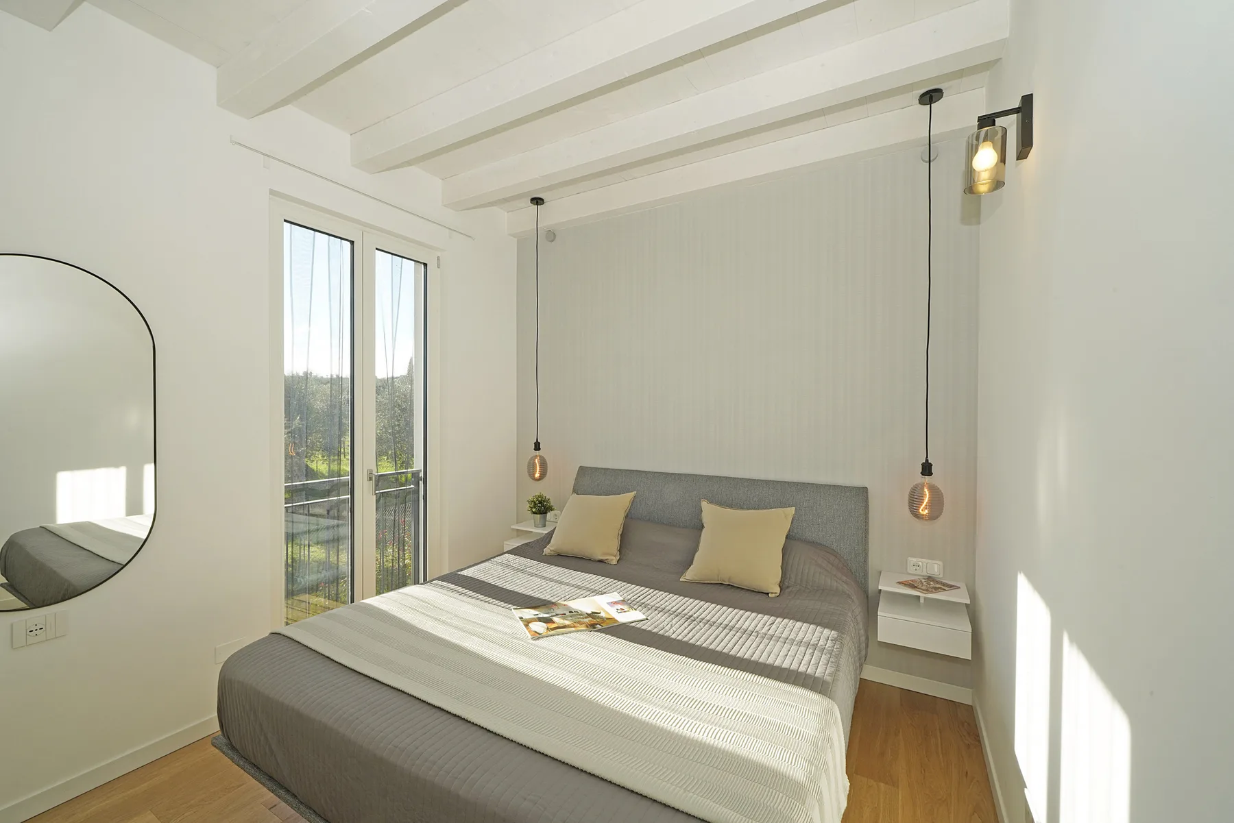 A bright bedroom with a neatly made bed and tall glass doors.