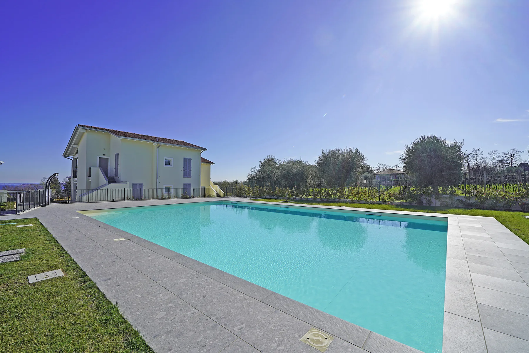 A swimming pool beside a two-story house under a clear blue sky.