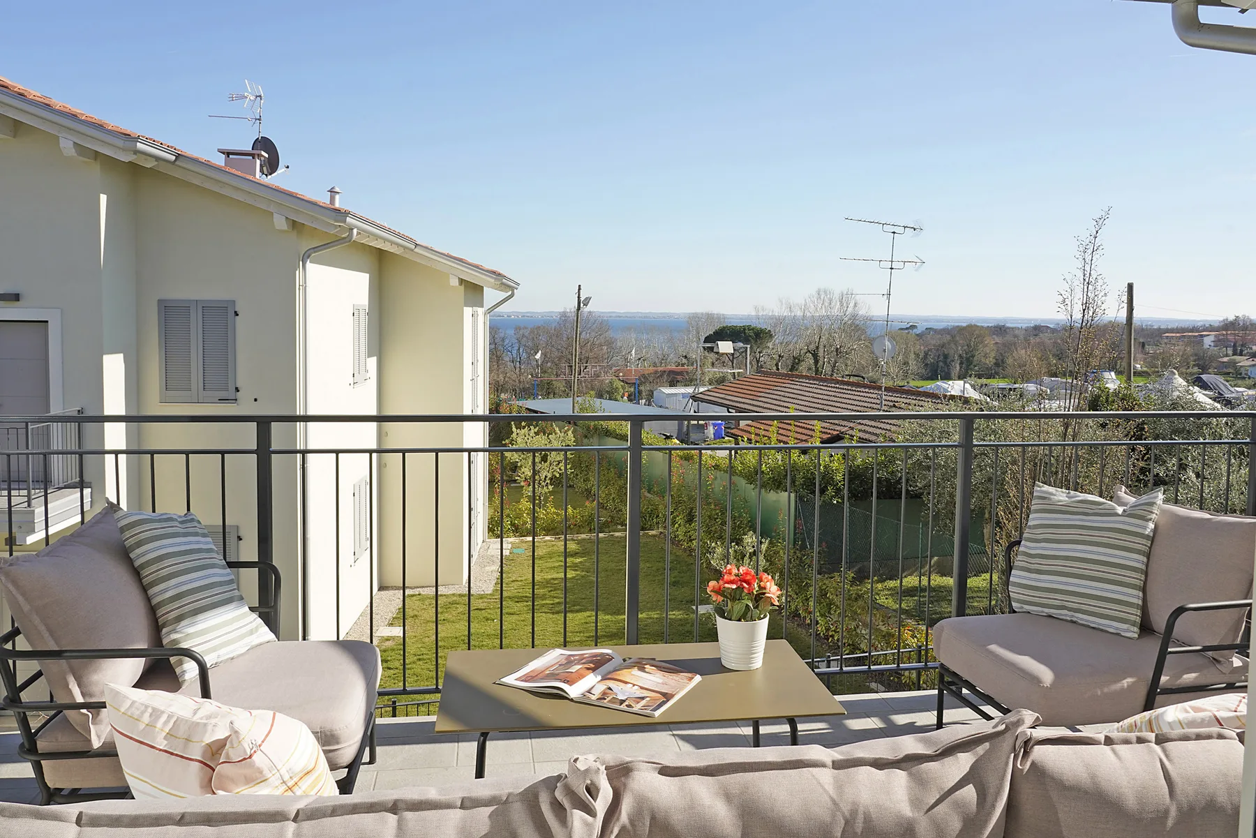 A sunny outdoor terrace with seating and a table overlooking a green landscape.