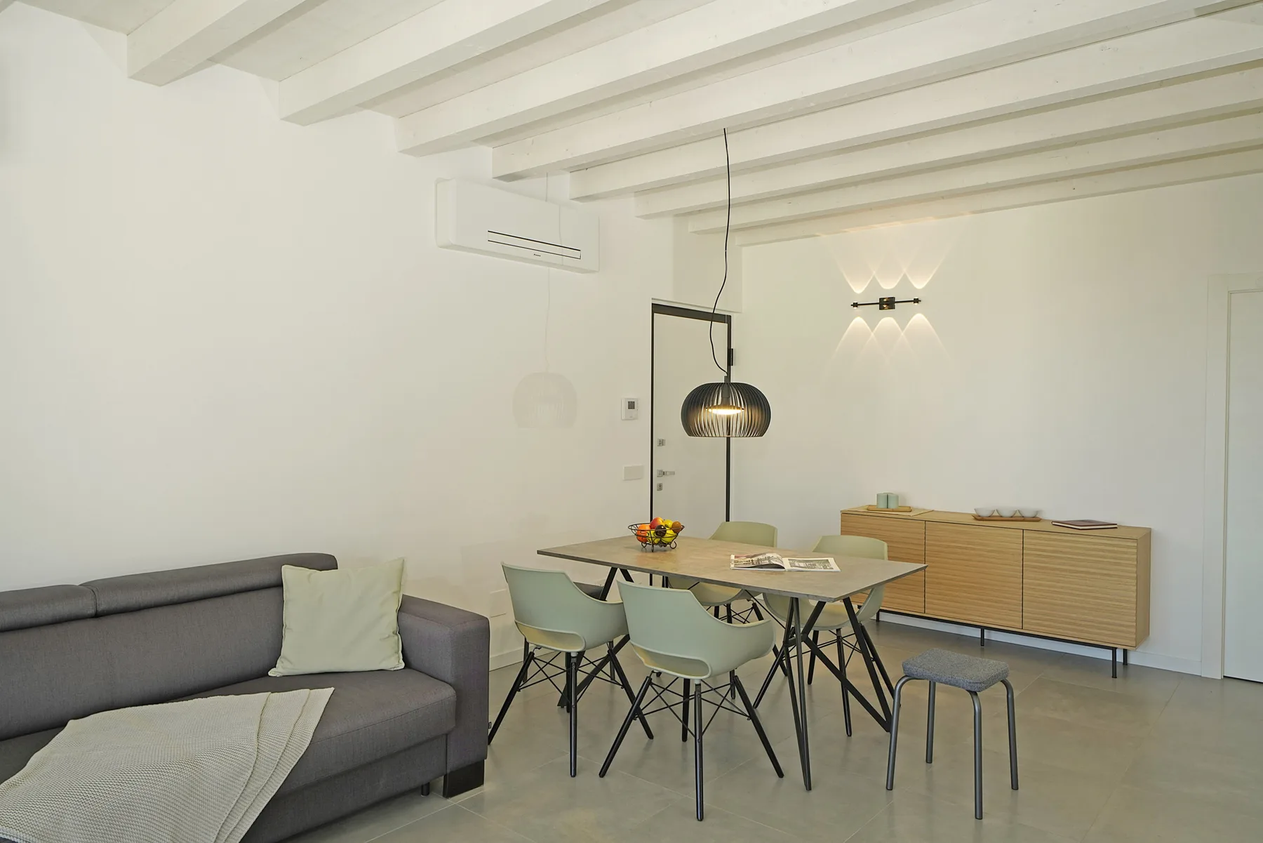 A bright dining area with a table and seating beside a gray sofa.