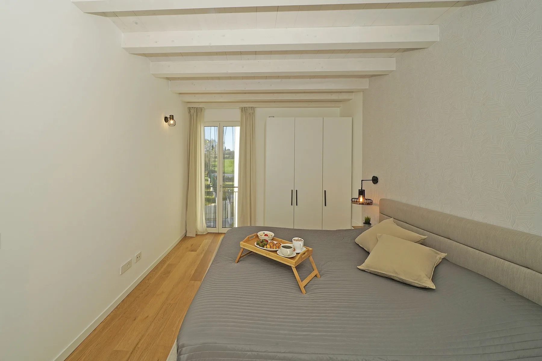 A bedroom with a large bed, a small table, and doors opening onto a balcony.