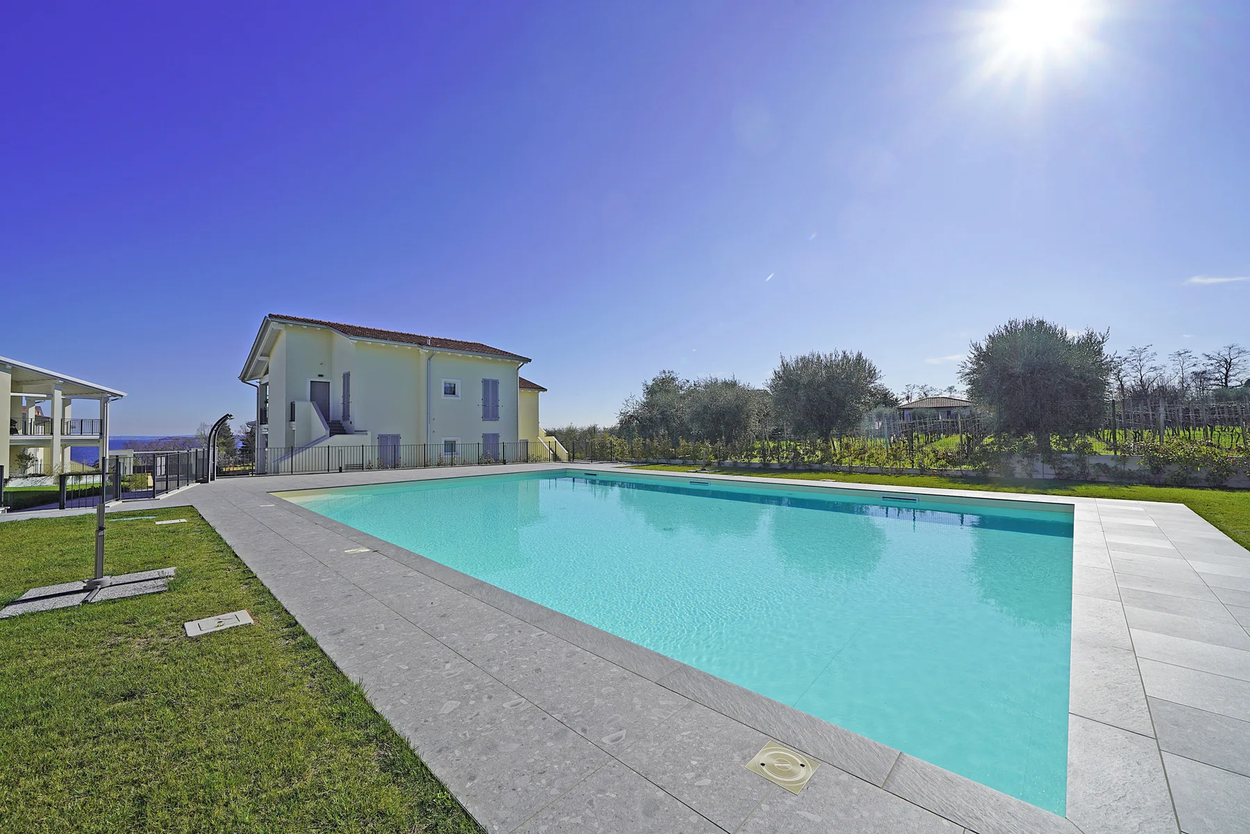 An outdoor swimming pool beside a pale two-story building and grassy lawn.