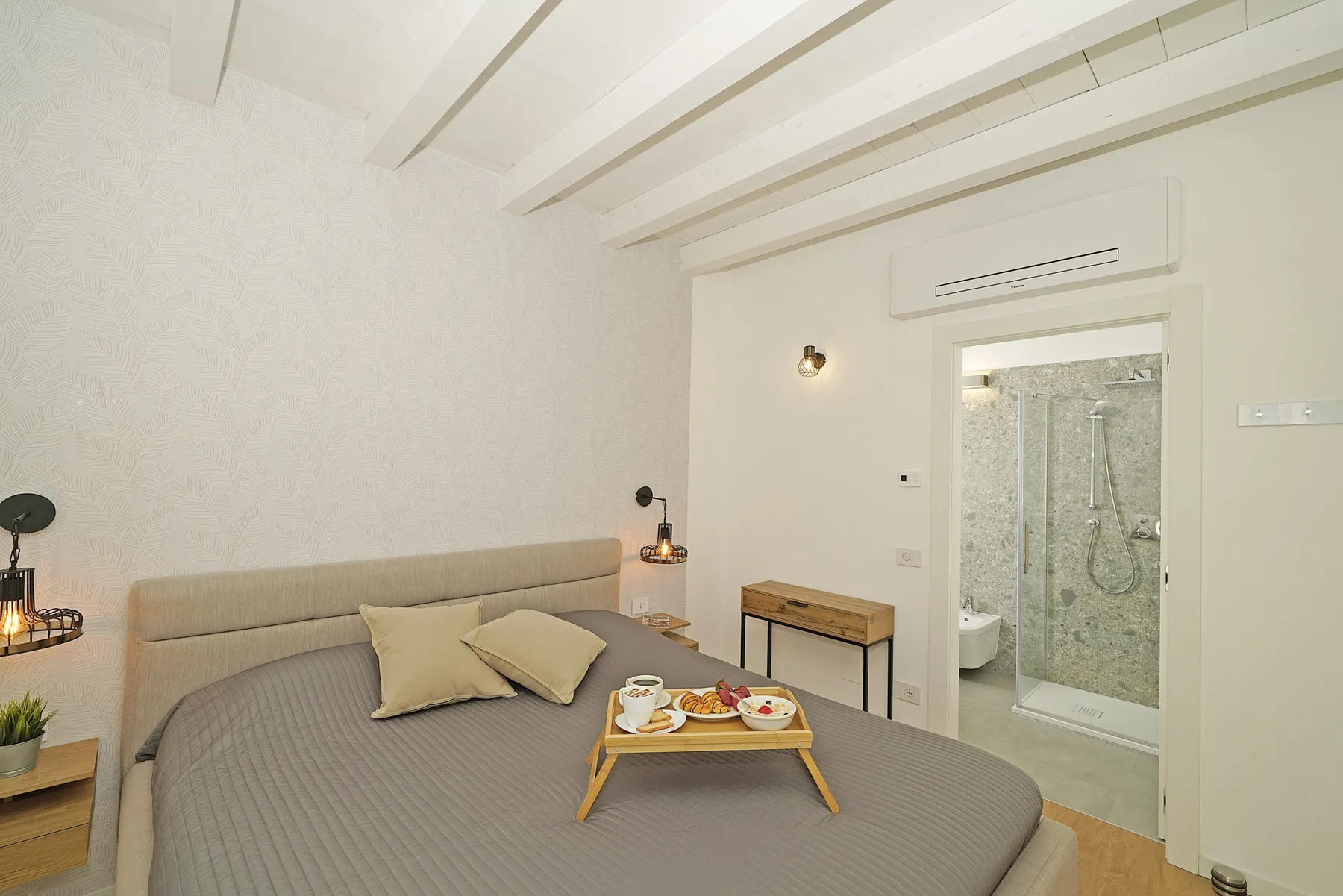 A bedroom with a bed and a small breakfast tray beside an open bathroom.