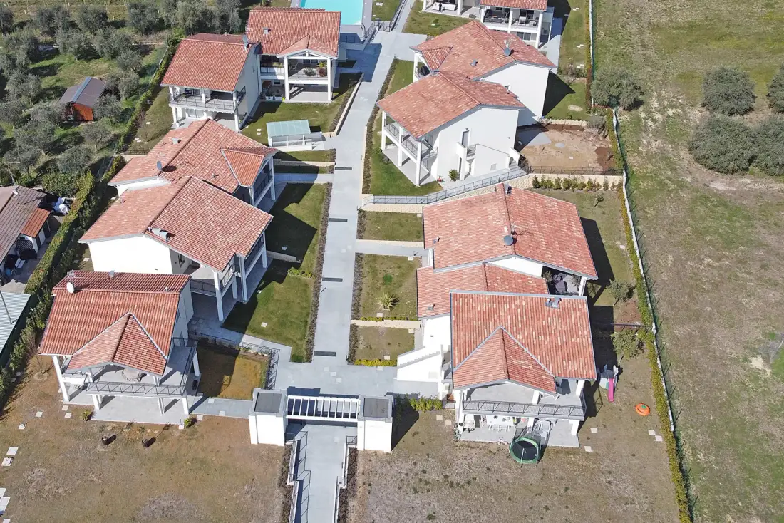 Aerial view of several houses along paved paths, surrounded by open grassy land.