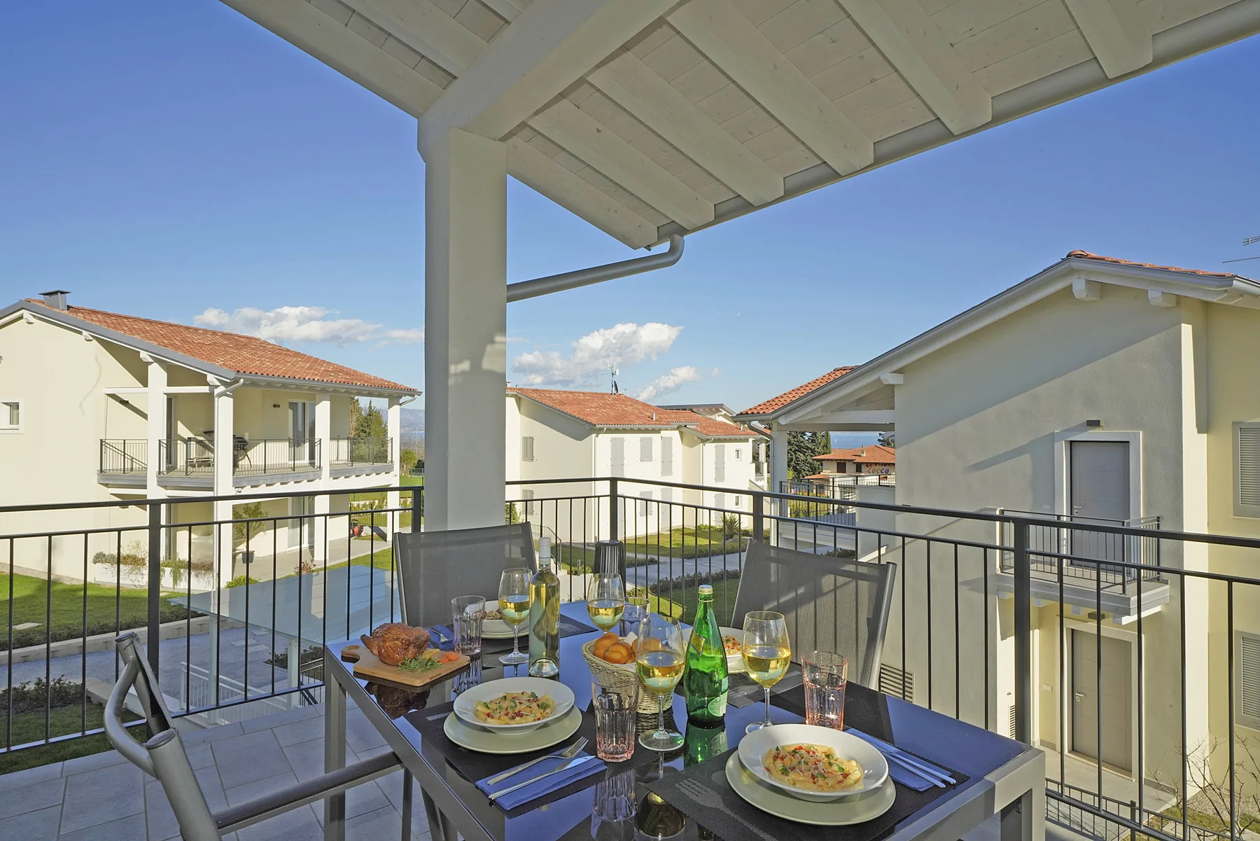 A covered balcony dining area overlooks nearby buildings under a clear sky.