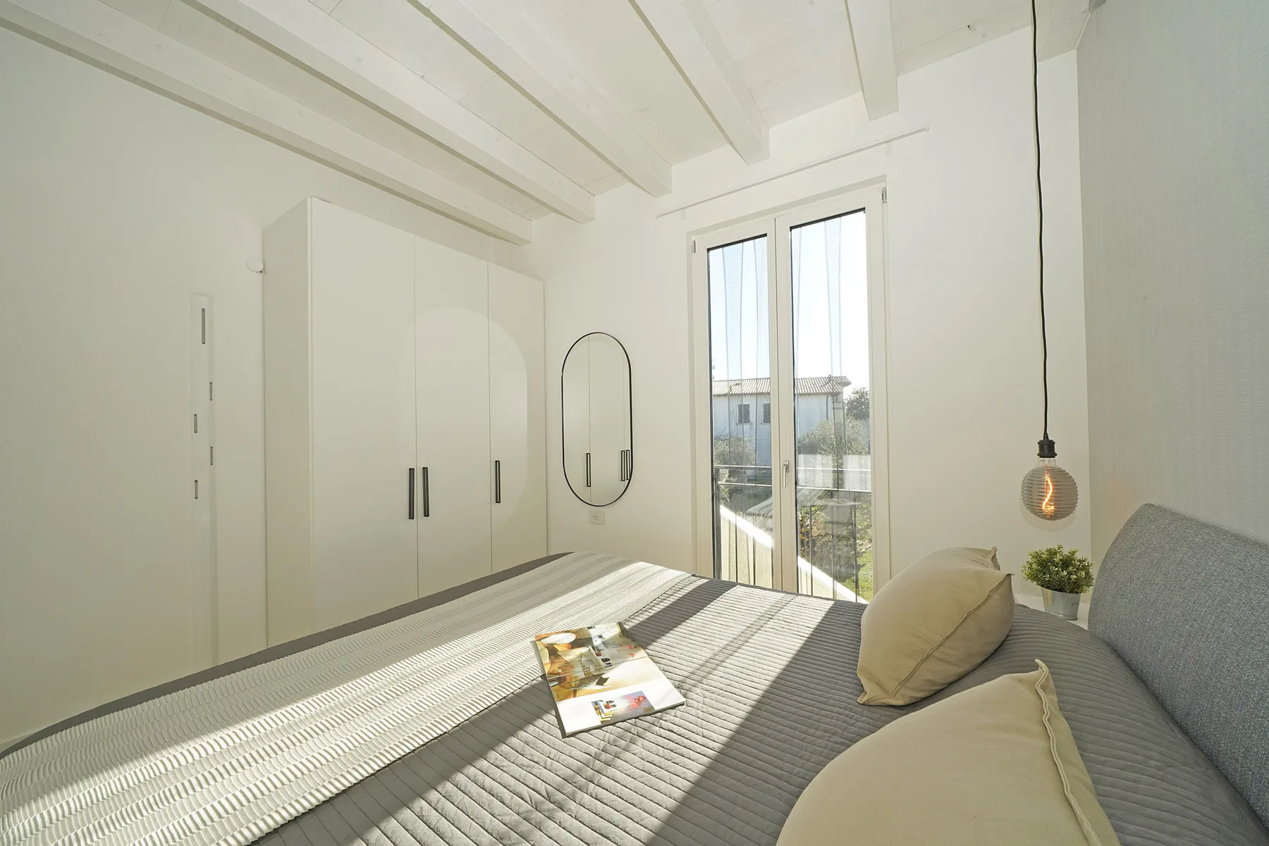 A bright bedroom with a bed beside a glass door opening onto a balcony.