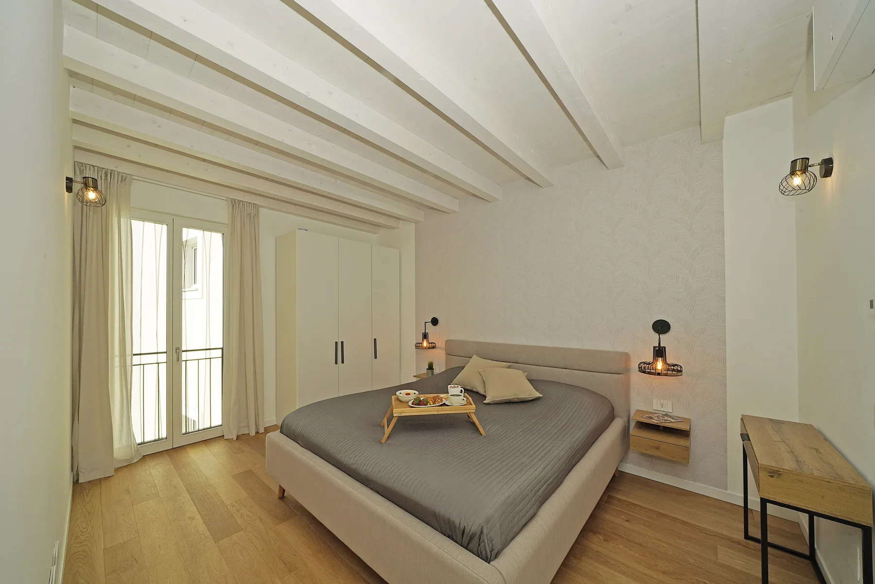 A bedroom with a large bed, bedside tables, and a tray on the bed.