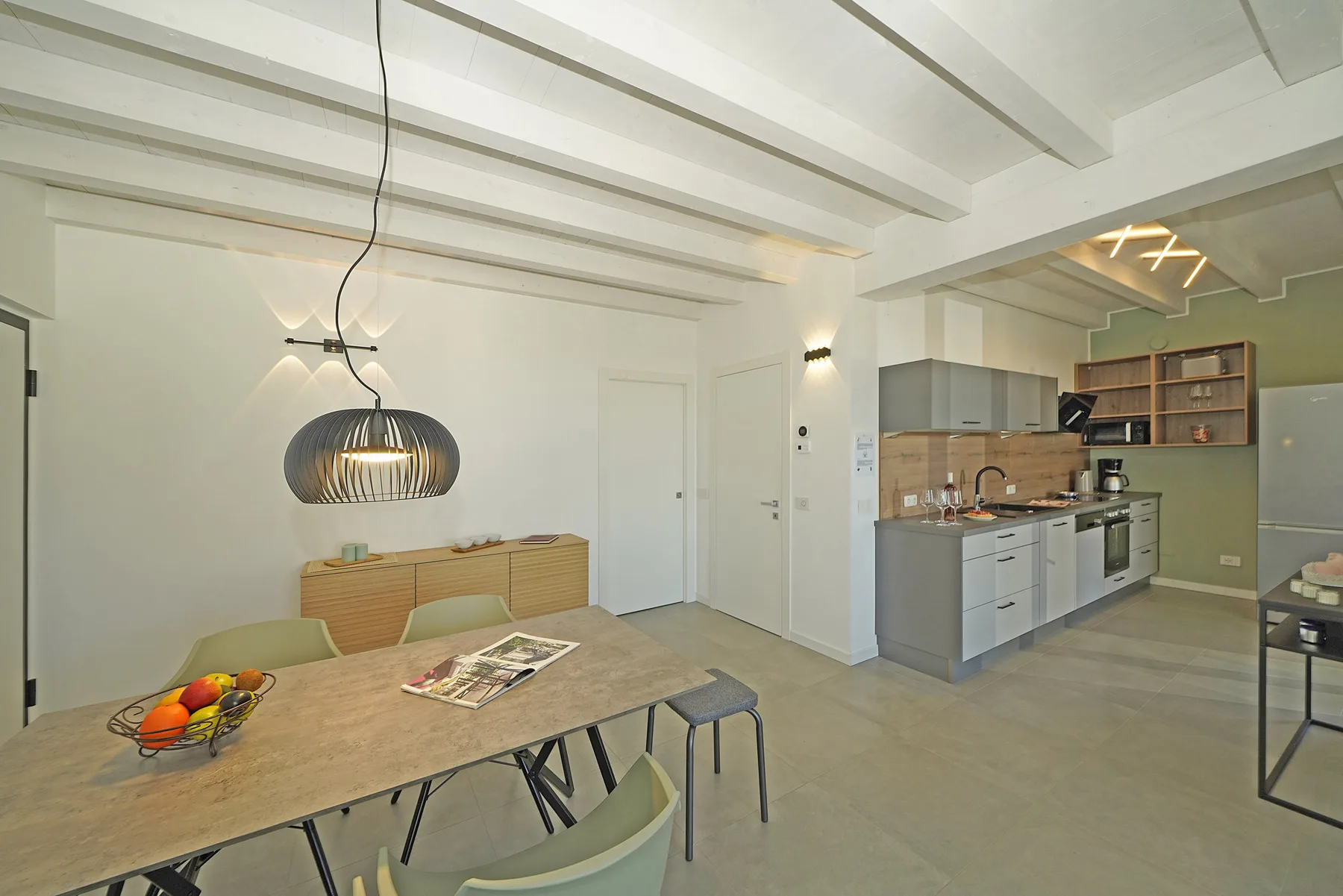 An open-plan dining and kitchen area with a table beneath exposed ceiling beams.