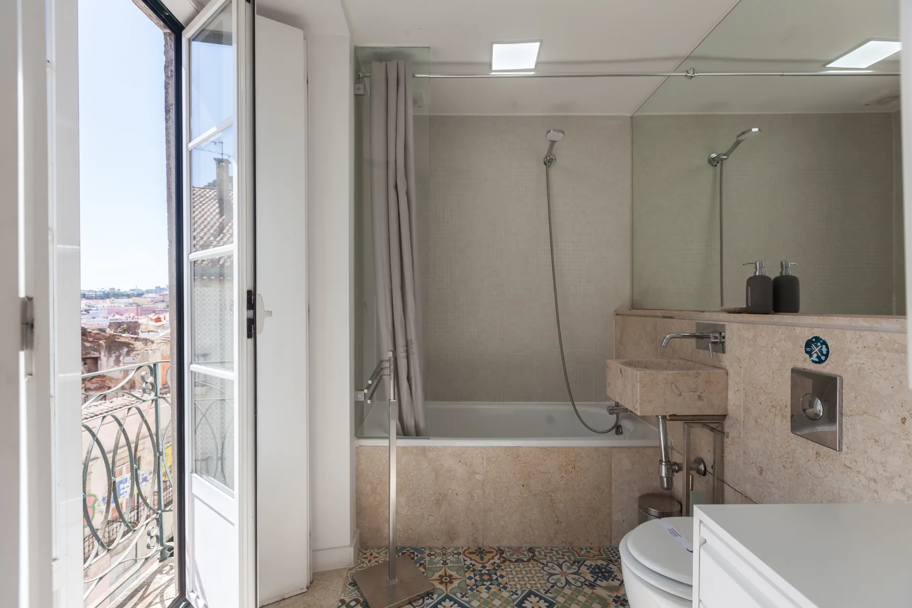 Un baño con ducha y una puerta abierta al balcón.