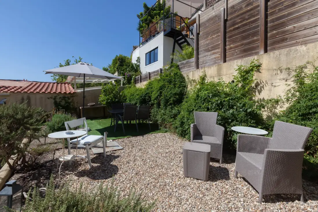 Un patio de grava con asientos al aire libre, vegetación y una gran sombrilla.