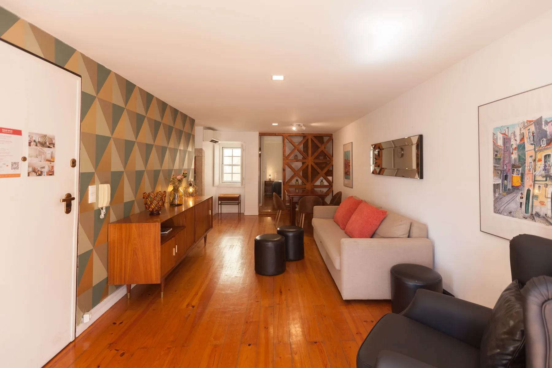 Una sala de estar con asientos, suelo de madera y papel tapiz geométrico.