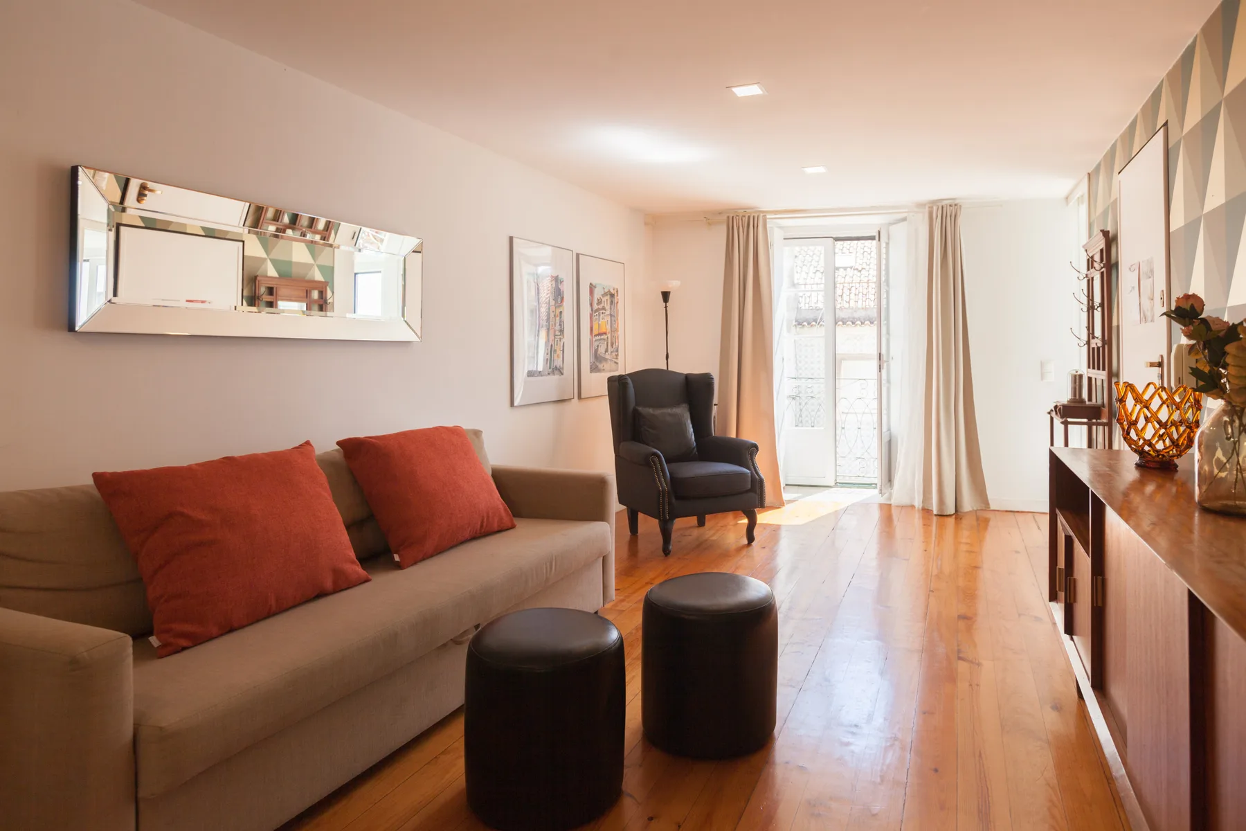 Una sala de estar con sofá, sillón y puertas de vidrio que dan a un balcón.
