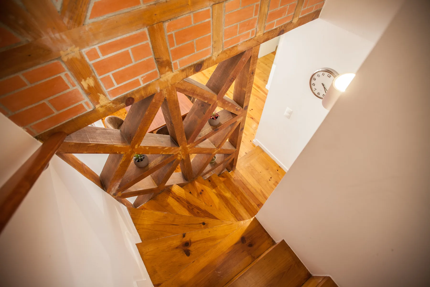 Una escalera de madera bajo vigas de madera y ladrillo visto.