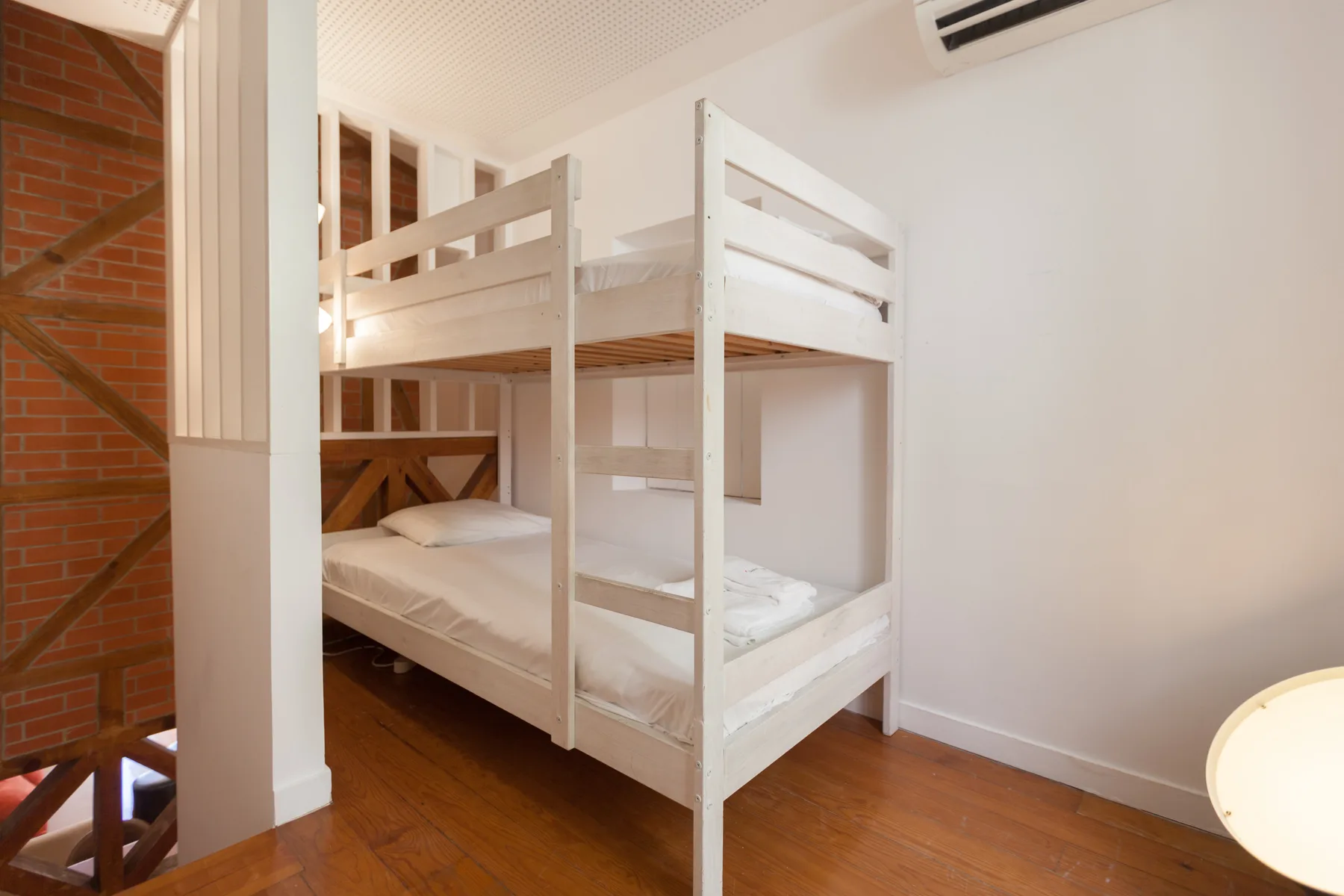 Un dormitorio con literas blancas y una pared de ladrillo.