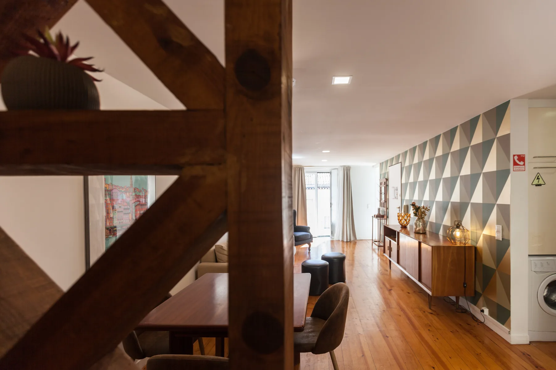 Sala de estar y comedor con suelo de madera y una pared geométrica decorativa.