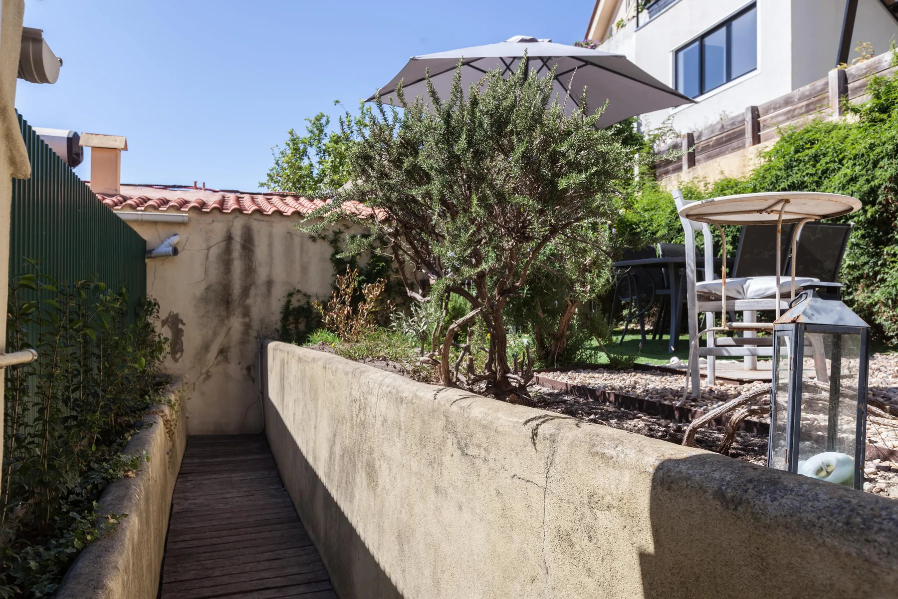 Una terraza ajardinada con un estrecho sendero de madera junto a jardineras elevadas.